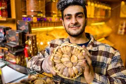 دانلود عکس با کیفیت فروشنده ترکیه ای در بازار در حال نشان دادن شیرینی سنتی ترکی