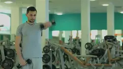 دانلود فوتیج مرد جوان در باشگاه بدنسازی در حال ورزش با دمبل