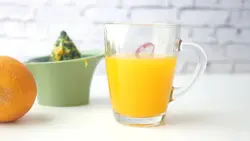 دانلود فوتیج لیوان آب پرتقال کنار آب میوه گیر دستی و پرتقال سالم روی میز