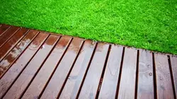 دانلود فوتیج باریدن قطره های باران روی کف چوبی و چمن تازه باغ