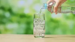 دانلود فوتیج بطری در دست در حال ریختن آب آشامیدنی در لیوان پر از تکه های یخ