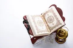 عکس با کیفیت تبلیغاتی قرآن بر روی رحل و فانوس کوچک در کنارش در زمینه سفید
