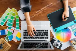 عکس با کیفیت تبلیغاتی دختر در حال نقاشی به کمک قلم نوری و لپ تاپ و جدول های رنگی و دوربین در کنارش