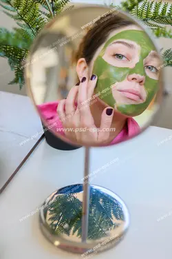 عکس با کیفیت تبلیغاتی تصویر زن در آینه و در حال گذاشتن ماسک سبز بر روی صورت