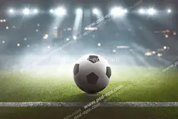 عکس با کیفیت تبلیغاتی توپ فوتبال در وسط زمین فوتبال زیر نور افکن ها