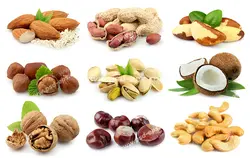 عکس با کیفیت انواع آجیل های مختلف اعم از بادام درختی ، بادام زمینی ، فندق ، پسته ، گردو ، بادام هندی و نارگیل قرار گرفته در یک صفحه به همراه برگ هایشان با زمینه سفید