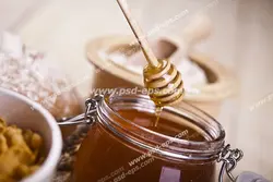 عکس با کیفیت شیشه عسل بر روی میز و برداشتن عسل از درون آن با قاشق مخصوص عسل