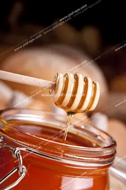 عکس با کیفیت برداشتن عسل از درون شیشه آن با قاشق مخصوص عسل از روی میز صبحانه