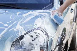 عکس با کیفیت شستشوی خودرو توسط کارگر کارواش با ابر پر از کف مواد شوینده