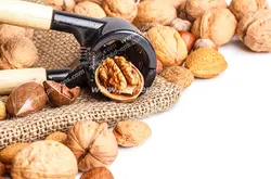 عکس با کیفیت گردوهای خشک در کنار دستگاه دستی گردوشکن بر روی کیسه و میز