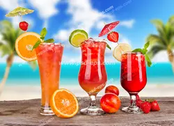 عکس با کیفیت لیوان و جام های بلور حاوی نوشیدنی های مختلف با تکه های میوه توت فرنگی و پرتقال و لیمو و هلو و نعنا با تزئین زیبا بر روی میز چوبی با پس زمینه از جزیره ای زیبا با آسمان آبی