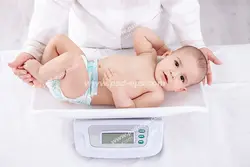 عکس با کیفیت نمای بالا از پزشک یا مسئول بهداشت در حال بررسی و سنجش وزن کودک و یا نوزاد با استفاده از وزنه مخصوص