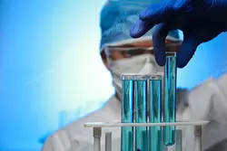 عکس با کیفیت متخصص علوم آزمایشگاهی در حال بررسی محتویات لوله آزمایش با زمینه آبی رنگ