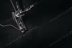 عکس با کیفیت نمای نزدیک از دوخت پارچه مشکی رنگ با چرخ خیاطی راسته دوزی