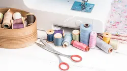 عکس با کیفیت ابزار خیاطی و جعبه نخ های رنگارنگ در کنار چرخ خیاطی سفید رنگ