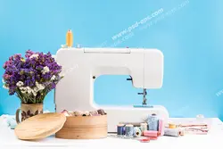 عکس با کیفیت چرخ خیاطی سفید در کنار گلدان گل و جعبه لوازم خیاطی