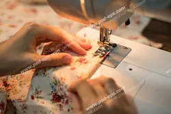 عکس با کیفیت بانوی خیاط در حال دوخت پارچه گل دار و طرح دار با چرخ خیاطی
