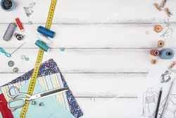 عکس با کیفیت پارچه های طرح دار و گل دار در کنار ابزار خیاطی و الگو و طرح لباس بر روی میز چوبی