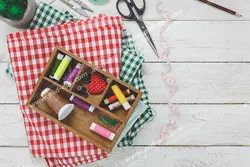 عکس با کیفیت جعبه وسایل و ابزار خیاطی از جمله قیچی ، نخ بر روی پارچه های چهارخانه قرمز و سبز رنگ بر روی میز چوبی ویژه استفاده در امور تبلیغاتی و تجاری طراحی کاتالوگ ، بروشور و تراکت با موضوع خیاطی ، تولیدی لباس ، آموزش خیاطی یا موسسات فنی و حرفه ای آموزش مقدماتی تا حرفه ای و لباس شب و لباس عروس