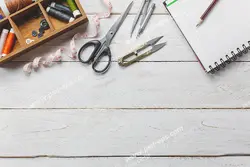 عکس با کیفیت جعبه وسایل و ابزار خیاطی از جمله قیچی ، نخ زن ، نخ متر و دفتر و مداد بر روی میز چوبی ویژه استفاده در امور تبلیغاتی و تجاری طراحی کاتالوگ ، بروشور و تراکت با موضوع خیاطی ، تولیدی لباس ، آموزش خیاطی یا موسسات فنی و حرفه ای آموزش مقدماتی تا حرفه ای و لباس شب و لباس عروس