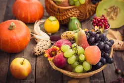 عکس با کیفیت سبدهای میوه های تازه و گل در کنار کدو تنبل با چیدمان زیبا مناسب تبلیغات شب یلدا بر روی میز چوبی